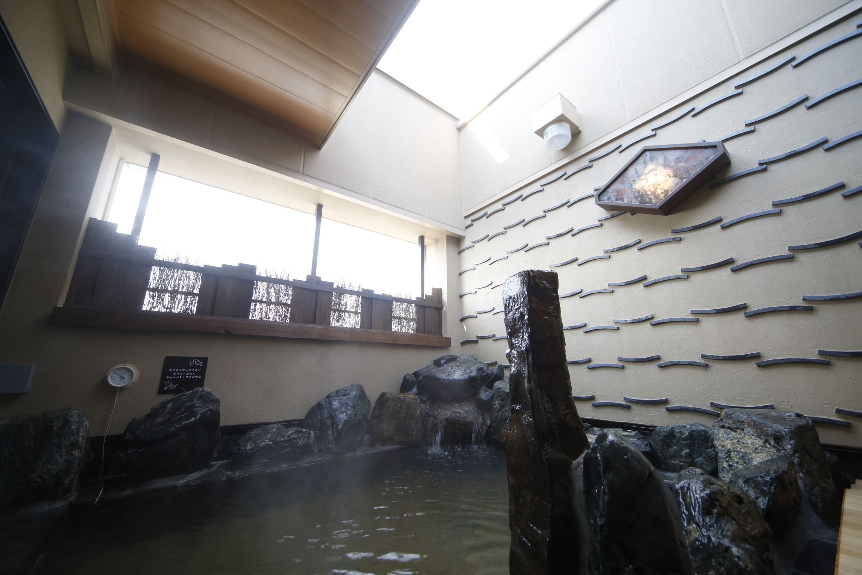 Un espace de bien-être comprenant une source d'eau chaude, des poutres en bois et un mur décoré de motifs de poissons.