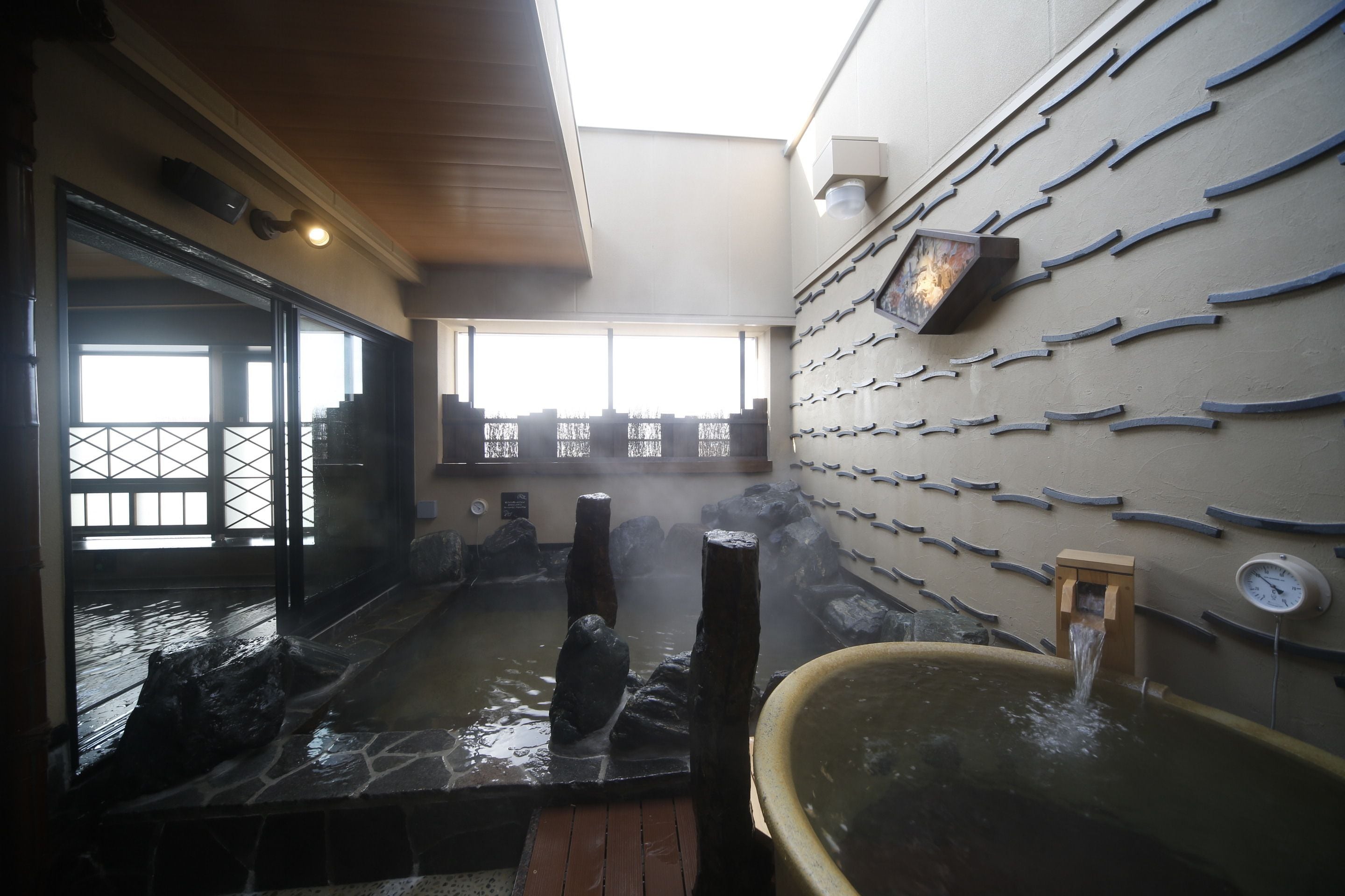 Un espace de baignade dans une source thermale, avec des marches en pierre, des poteaux en bois et une horloge fixée au mur.