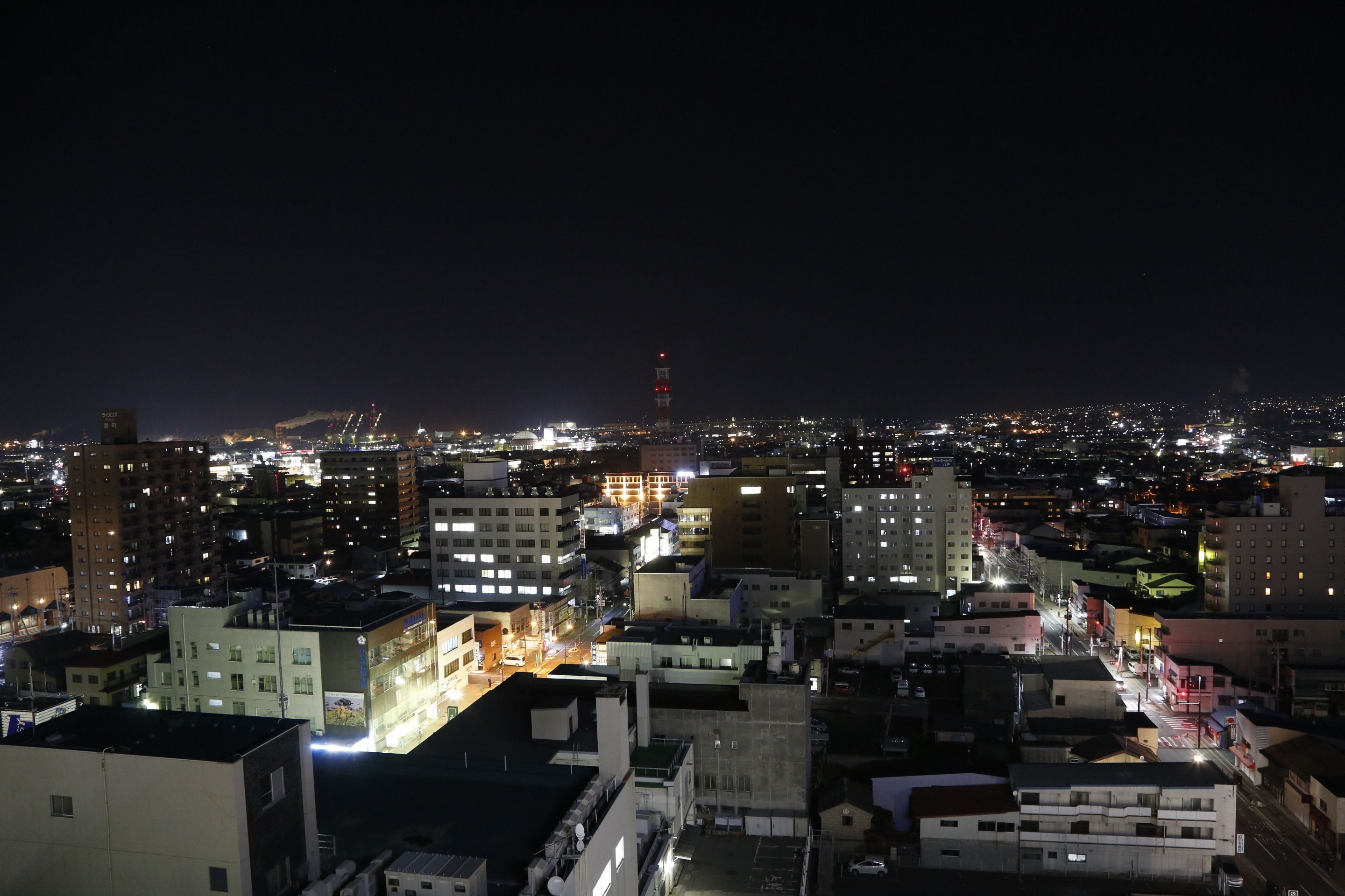 Eine beleuchtete Stadtlandschaft bei Nacht mit Gebäuden und einem markanten Turm in der Ferne.