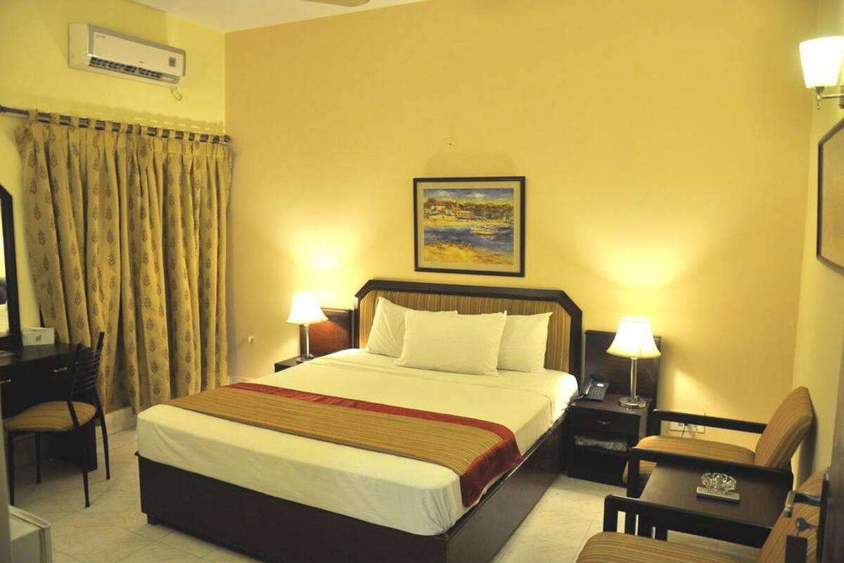Habitación de hotel con una cama grande, dos mesitas de noche con lámparas, un escritorio con silla y un cuadro en la pared.