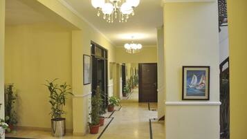 A hallway with potted plants, a chandelier, and framed artwork on the walls.