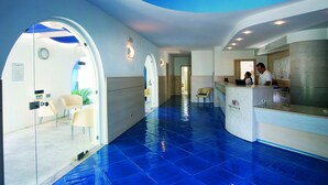 A hotel lobby with a blue-tiled floor, a reception desk, and a waiting area with chairs. - Futura Club Torre Rinalda (Lecce)