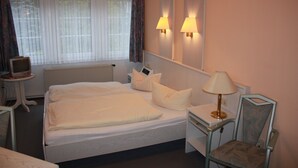 A hotel room with a large bed, bedside lamps, a desk with a lamp, a chair, and a television on a small table. - Misselhorner Hof (Südheide)