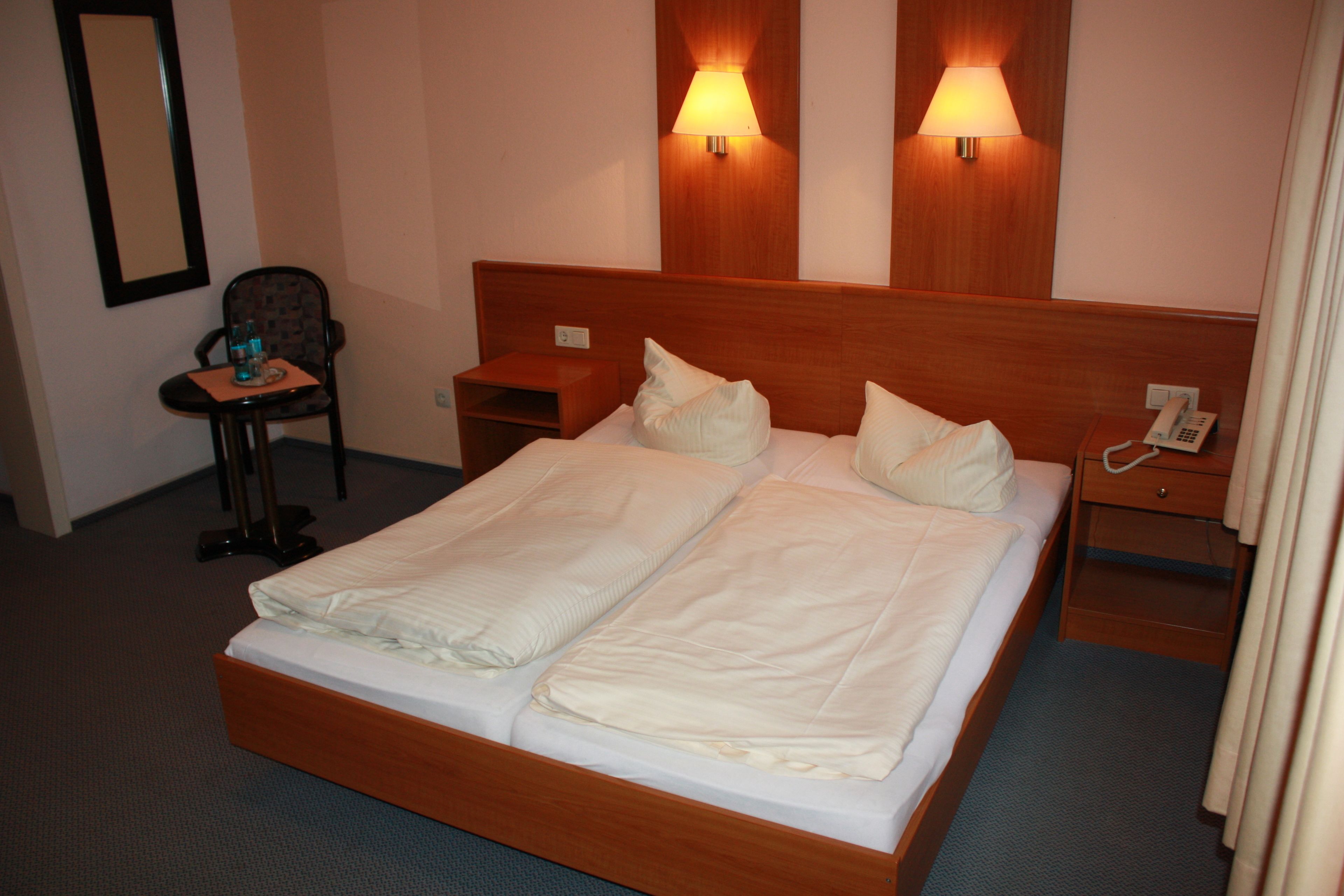 Ein Hotelzimmer mit einem Doppelbett, zwei Nachttischen, einem Sessel, einem Schreibtisch und zwei Wandleuchten.