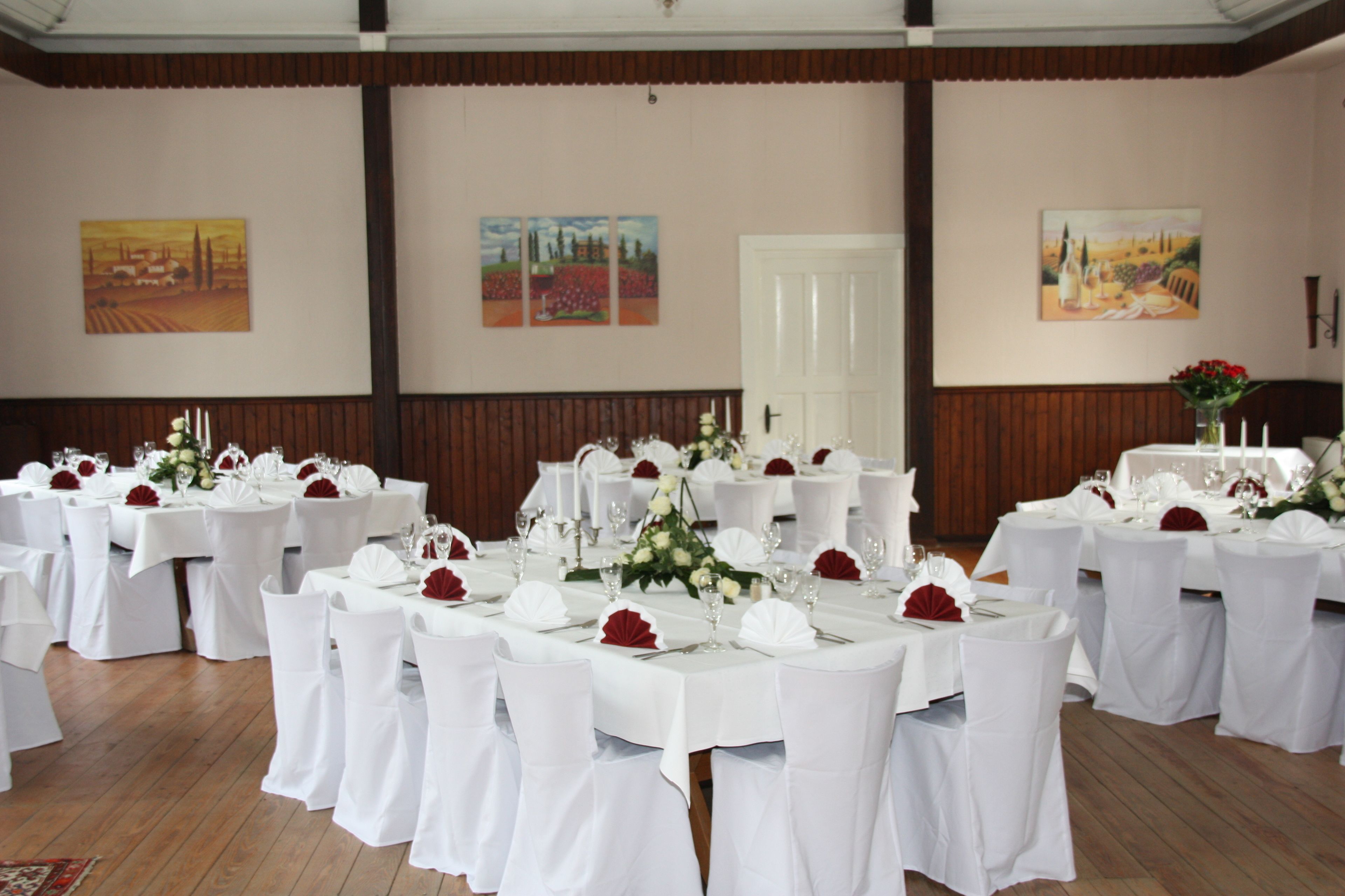 Une salle de banquet avec des tables rondes dressées pour un événement formel, des nappes blanches et des centres de table floraux rouges.