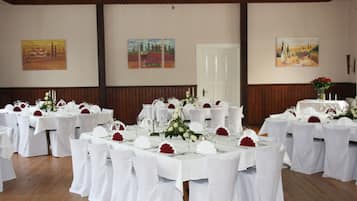 Un salón de banquetes con mesas redondas dispuestas para un evento formal, manteles blancos y centros de mesa florales rojos.
