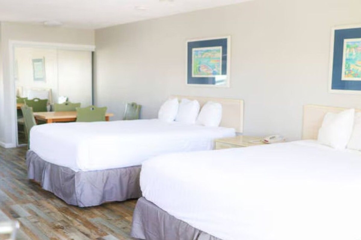A hotel room with two beds, a desk, and a chair. There are framed pictures on the walls.