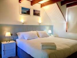 Habitación de hotel con una cama, dos lámparas de noche, una mesita de noche y dos cuadros en la pared.