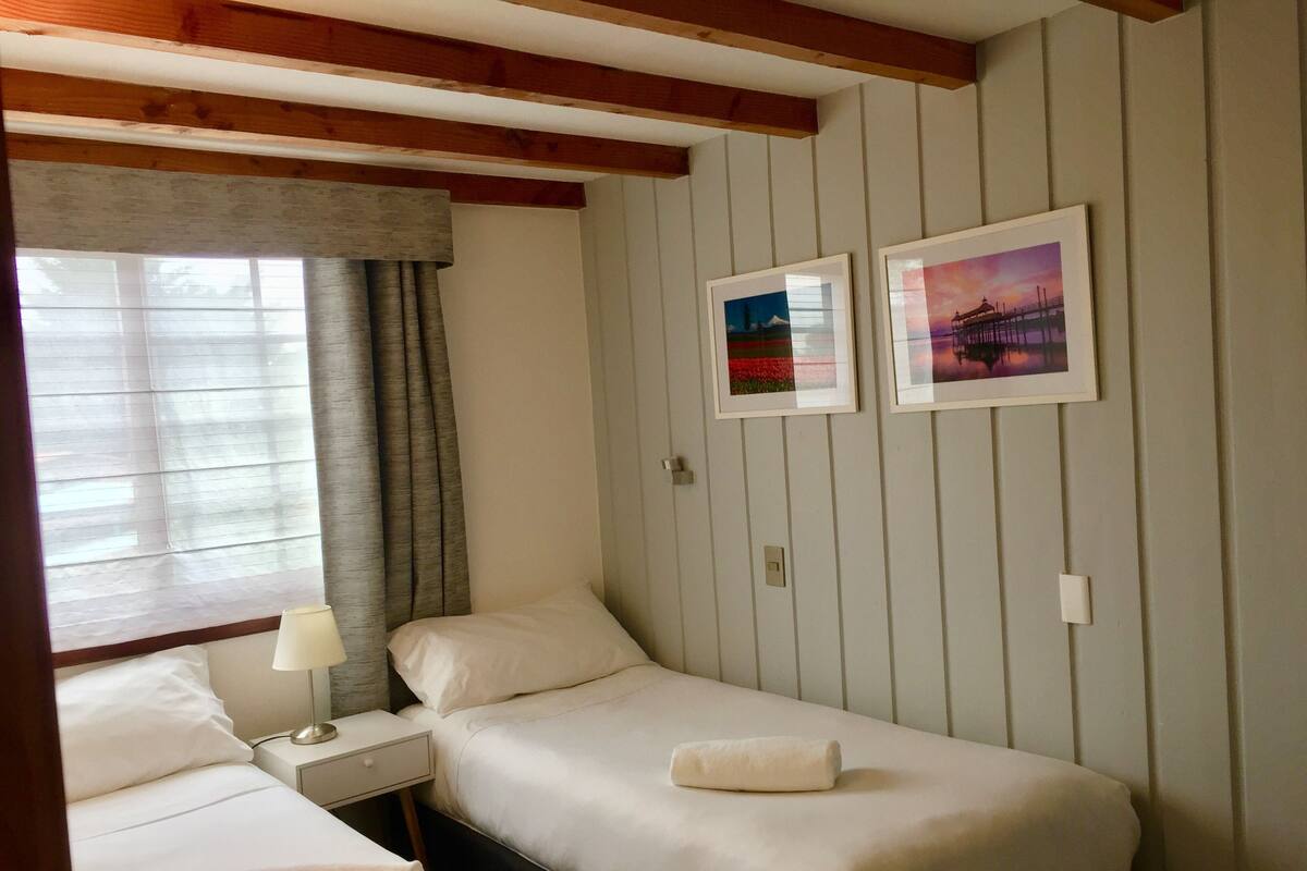 A hotel room with two single beds, a nightstand with a lamp, and two framed pictures on the wall.