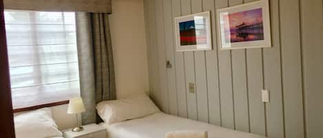 A hotel room with two single beds, a nightstand with a lamp, and two framed pictures on the wall.