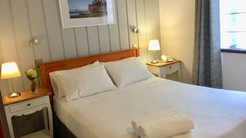 A neatly made bed with white linens, two bedside tables with lamps, a framed picture on the wall, and a window with curtains.