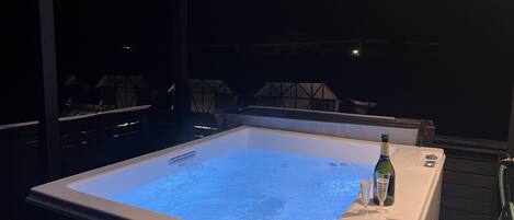A hot tub with a blue water surface, a bottle, and two glasses on a table.