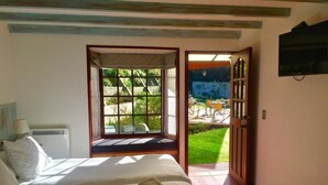 A hotel room with two beds, a TV, and a view of a garden and outdoor seating area. - Hotel Frutillar (Frutillar)