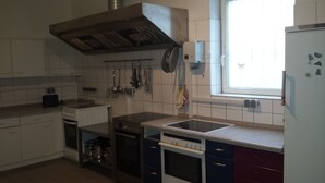 A kitchen with white cabinets, a stainless steel range hood, a window with a view, and a refrigerator with magnets. - Gästehaus Vienenburg (Goslar)