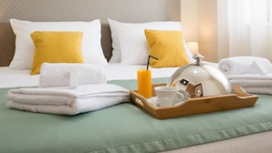 Una cama bien tendida con almohadas blancas y amarillas, una bandeja con una taza, un vaso de zumo de naranja y una toalla blanca.