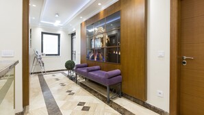 Un área de recepción con un mostrador de madera, un sofá púrpura, una vitrina de vidrio y un piso de mármol.
