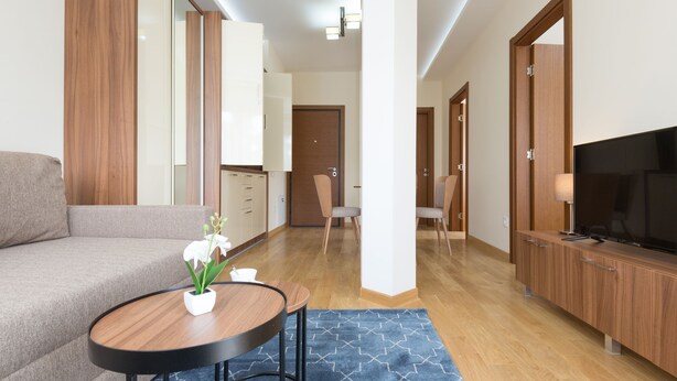 Una sala moderna con sofá, mesa de centro y televisión. Se observa un mueble de madera y una puerta al fondo.