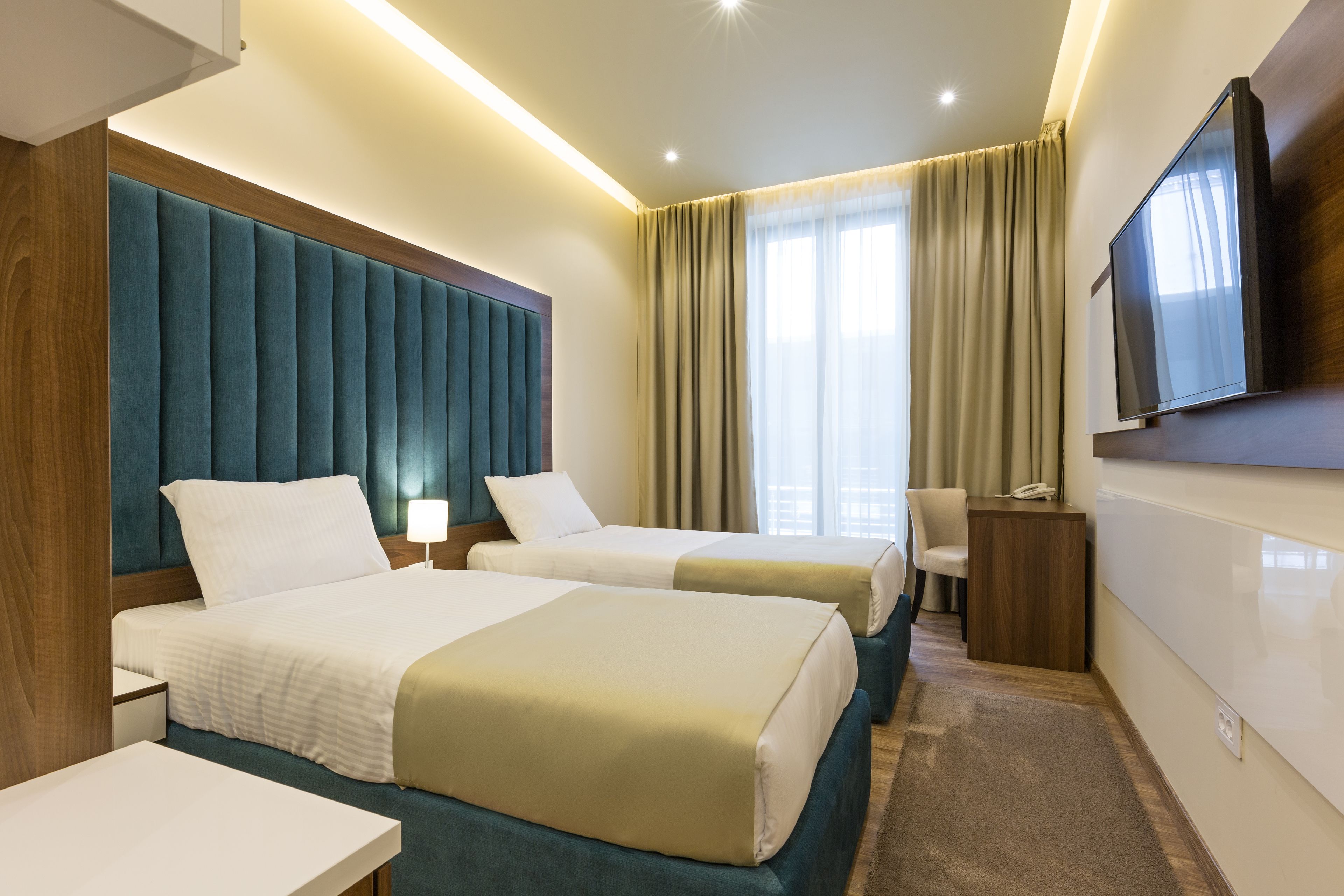 A hotel room with two beds, a desk, a chair, a TV, and a window with curtains.