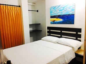 Cama com roupa de cama branca, cabeceira preta e um quadro de um barco em um mar azul.