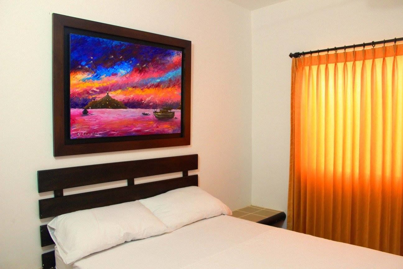 Quarto com cama, pintura de um pôr do sol sobre a água e cortina.