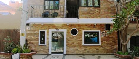 A two-story building with a brick facade, a balcony with chairs, and a sign indicating a restaurant.
