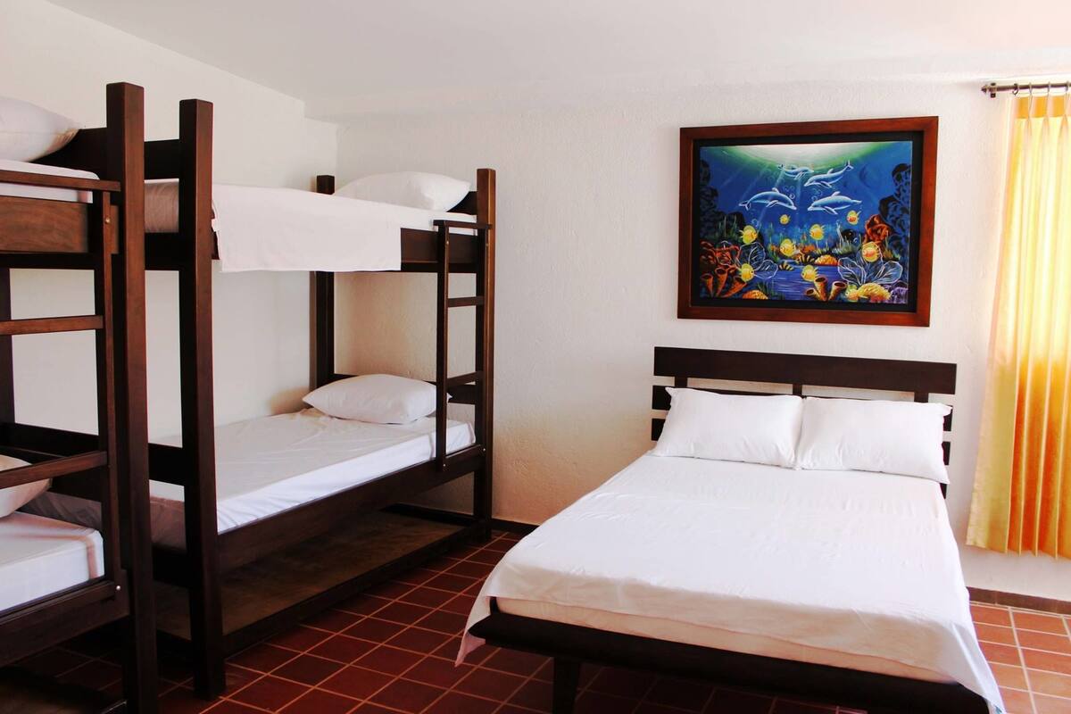 A room with two bunk beds and a single bed, a painting of an underwater scene, and a window with curtains.