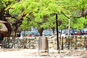 A stone wall with a metal chair in front, a thatched-roof building, and a view of boats in the background. - San Marcos Taganga - Hostel (Santa Marta)