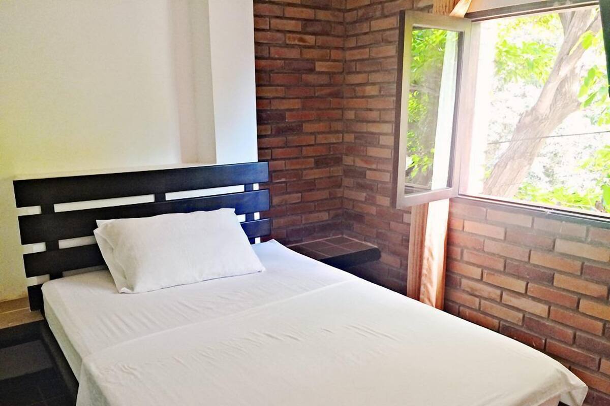 A single bed with a black headboard in a room with brick walls and a window.