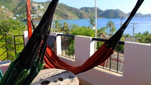 En hængekøje på en balkon med udsigt over et kystlandskab med bakker og vand.