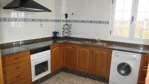 Una cocina con armarios de madera, horno empotrado, lavadora y ventana con vistas.