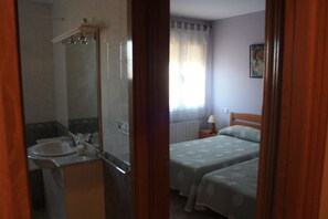 A bedroom with two beds, a bathroom with a sink, and a window with curtains. - Casa Cabriel (Villargordo del Cabriel)
