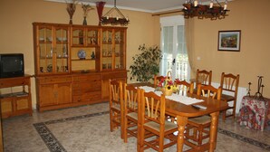 Un comedor con mesa y sillas de madera, un armario con puertas de vidrio y un televisor a la izquierda.