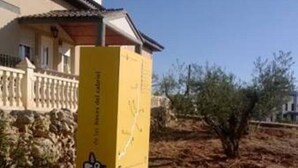 Un letrero amarillo con un mapa y texto, situado en una zona árida y despejada con vegetación escasa y un edificio al fondo.