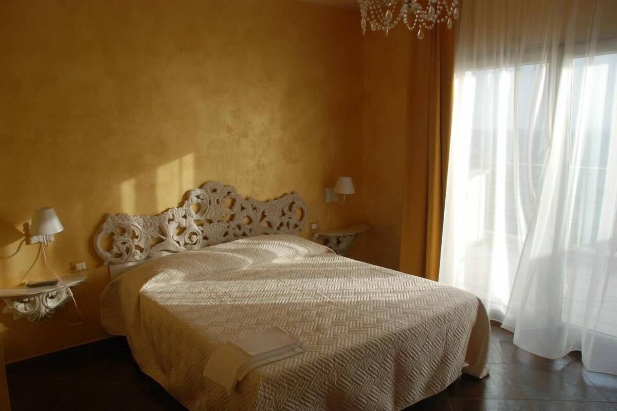 Ein Schlafzimmer mit einem großen Bett, einem verzierten Kopfteil, zwei Nachttischen mit Lampen und transparenten Vorhängen.