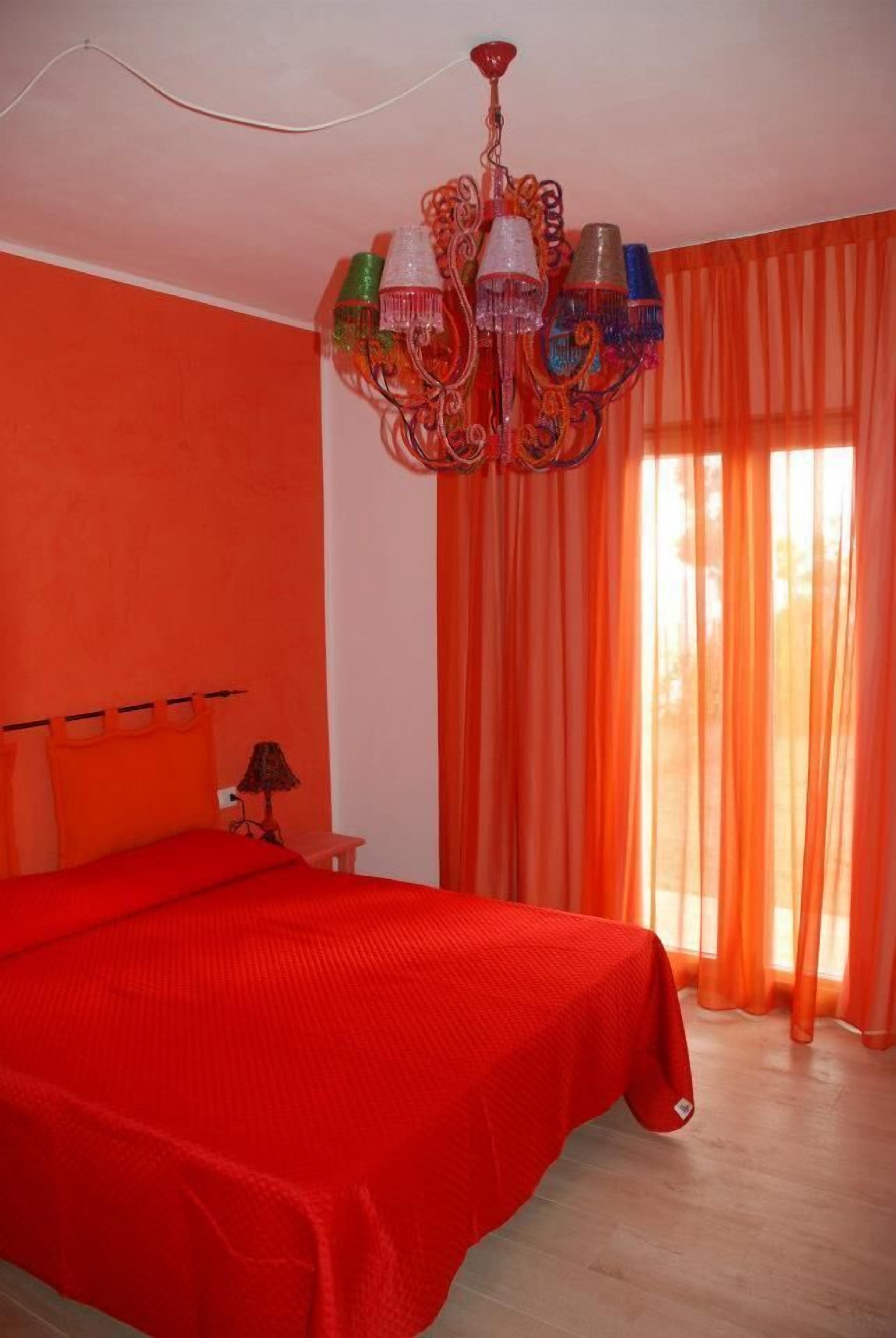 Une chambre avec un grand lit, des rideaux orange et un lustre.