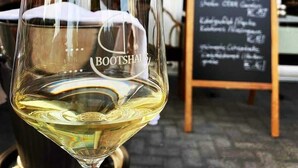 A glass of white wine on a table with a chalkboard menu in the background. - Hotel Restaurant Bootshaus (Achim)