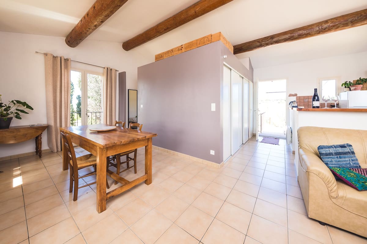 Un vaste espace de vie comprenant un coin repas avec une table en bois, un canapé et une cuisine équipée d’un comptoir et d’appareils électroménagers.
