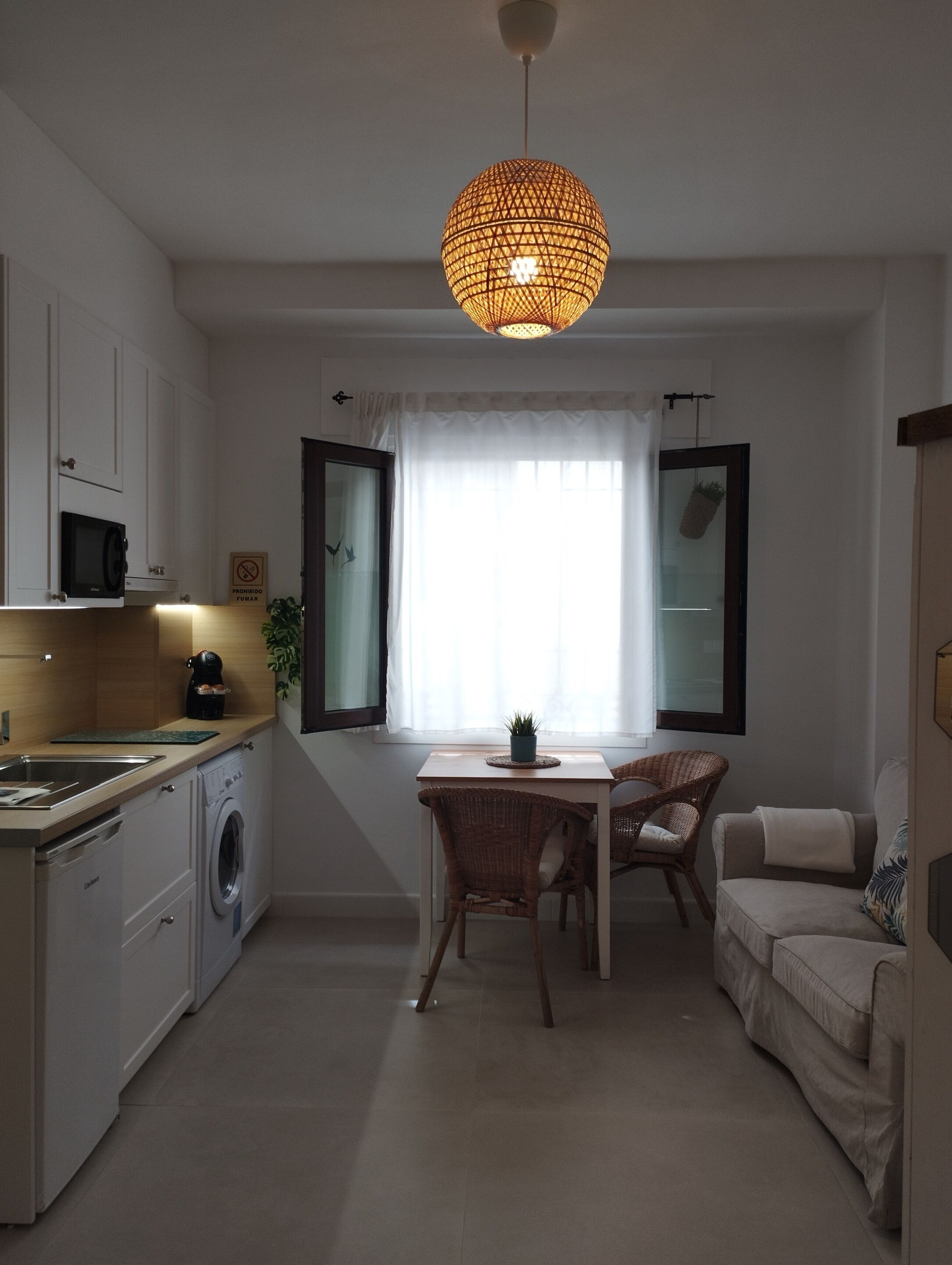 Une cuisine compacte équipée d’un four à micro-ondes, d’un lave-linge et d’un luminaire suspendu.