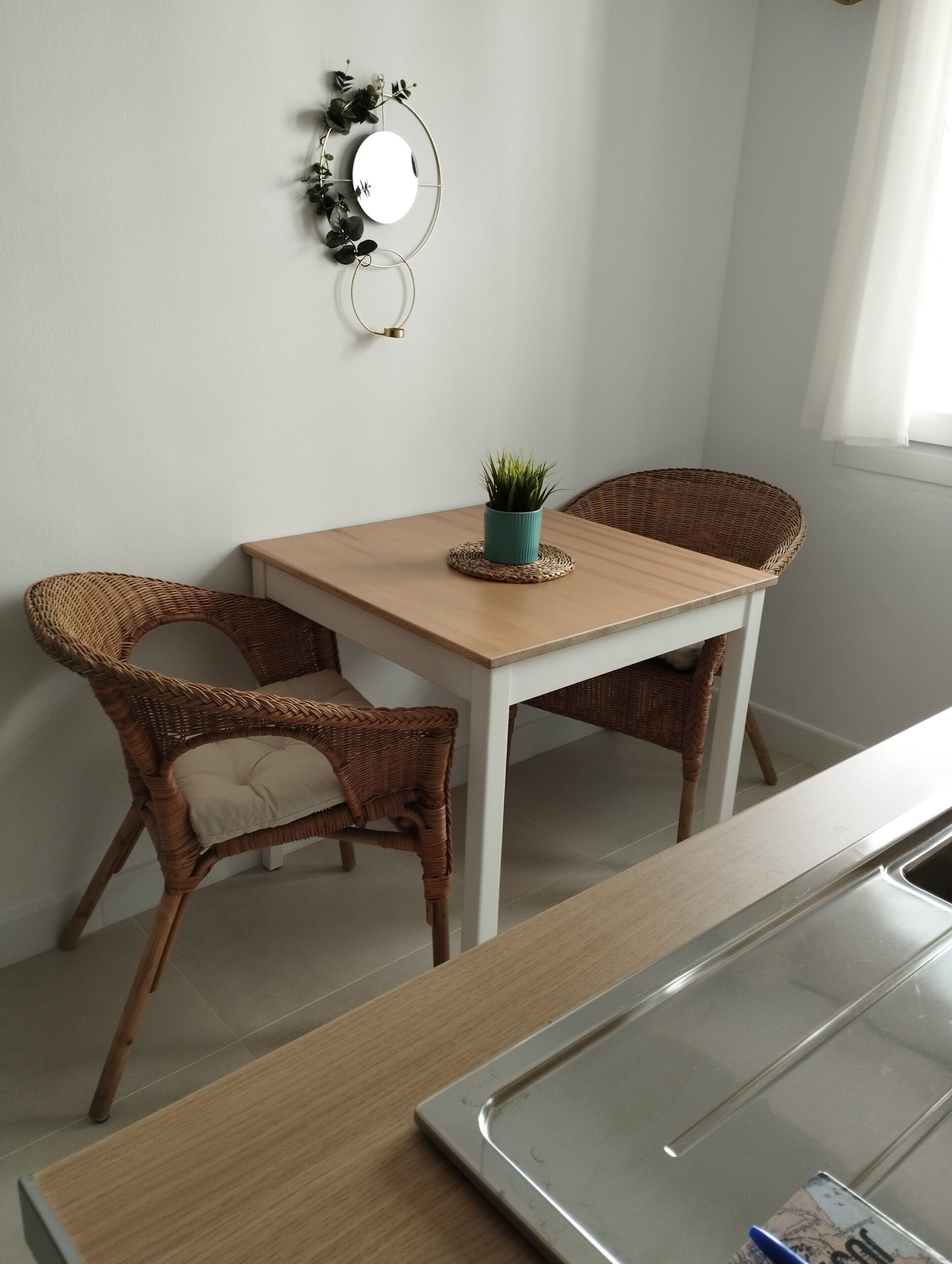 A dining area with a wooden table and wicker chairs, a small potted plant, and a wall-mounted mirror.
