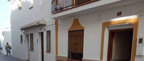 A street with a building featuring a balcony with metal railings, a tiled entrance, and a door marked with the number 68.