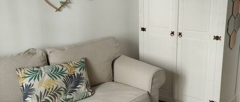 A neutral-toned living room with a beige sofa, a wicker chair, and a white wardrobe with decorative handles.
