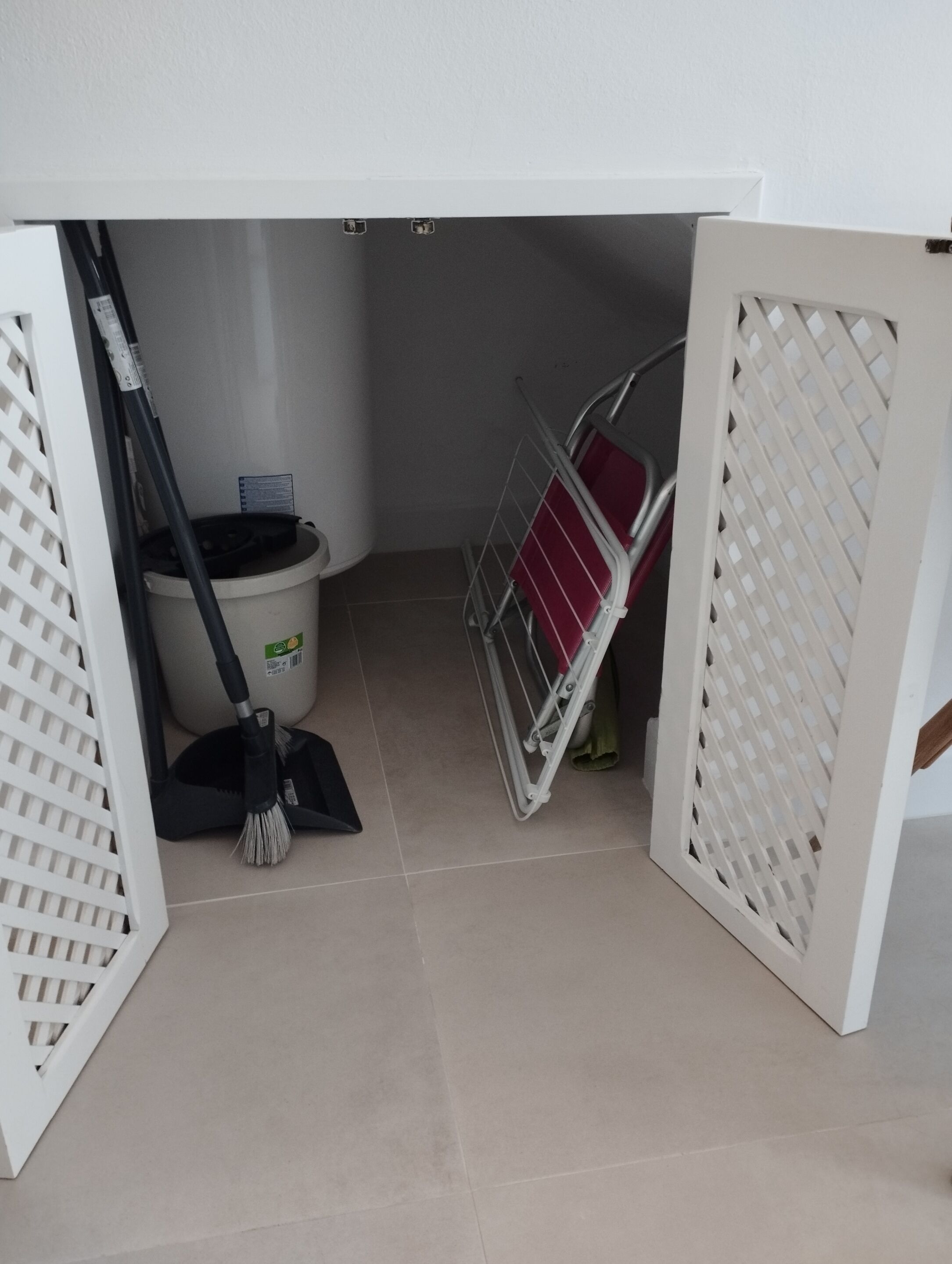 Un espacio de almacenamiento con un trapeador, un recogedor y una cesta de ropa.