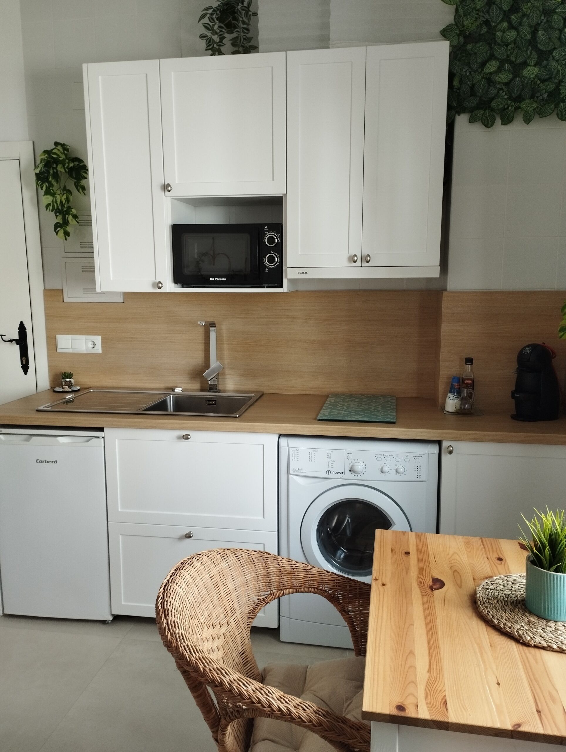 Une cuisine compacte avec des meubles blancs, un four à micro-ondes, un évier, un lave-vaisselle et une machine à laver.