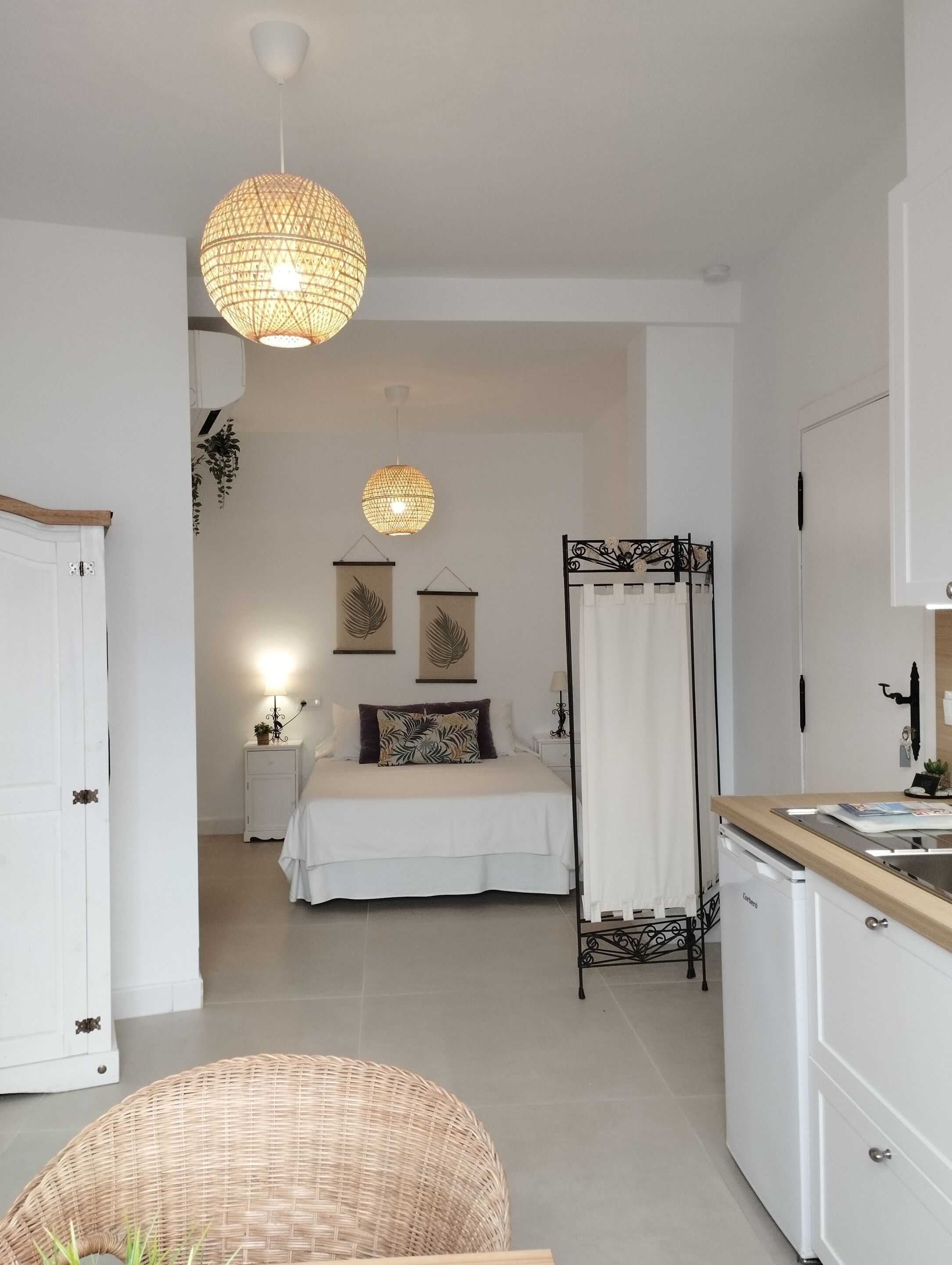 A bedroom with a bed, bedside tables, a hanging light fixture, and a view into the adjacent bathroom.