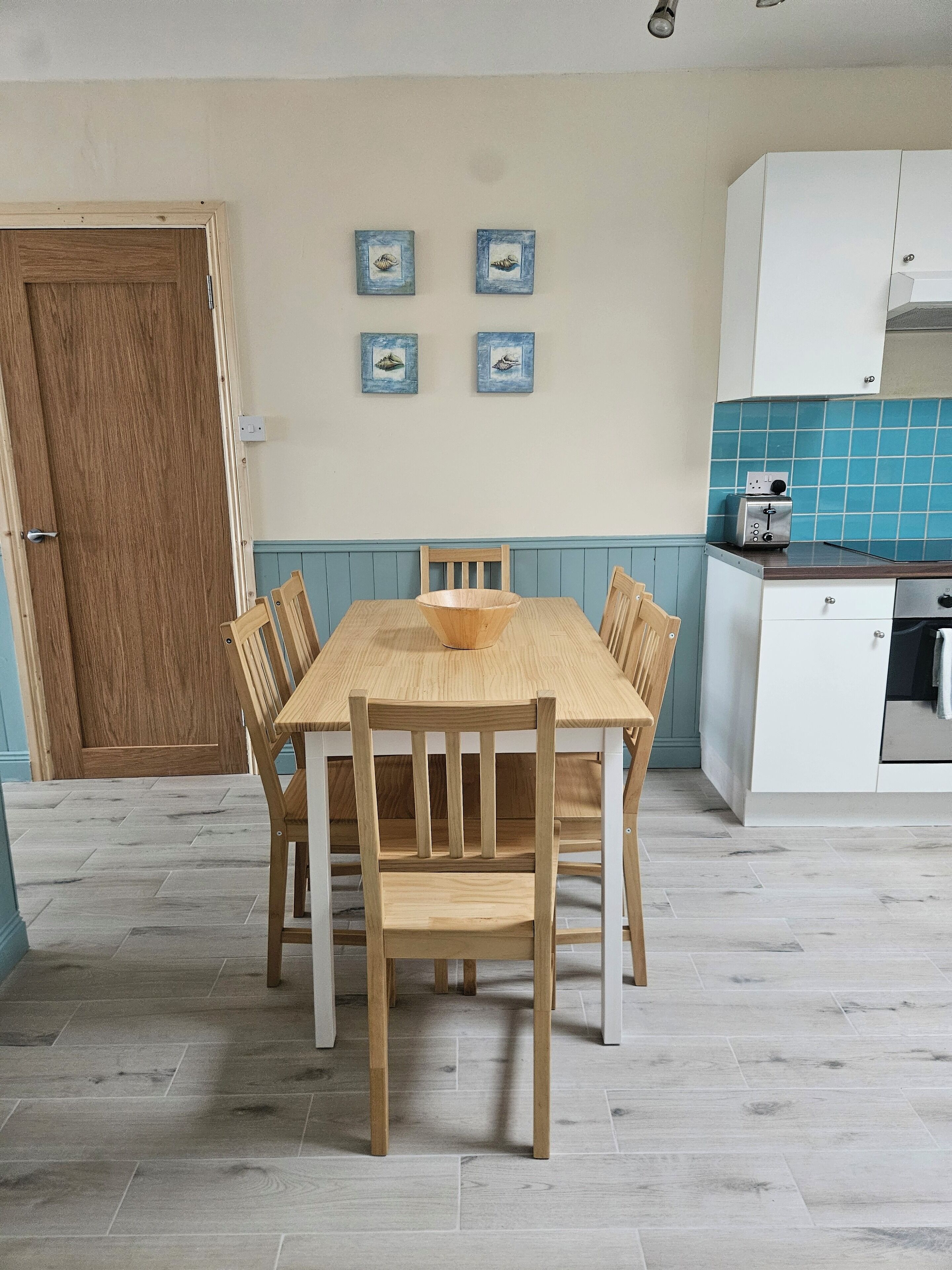 A dining area with a wooden table and chairs, a wooden door, and a kitchen with a toaster.