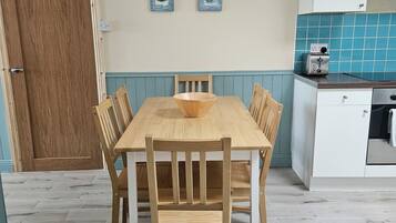 A dining area with a wooden table and chairs, a wooden door, and a kitchen with a toaster.