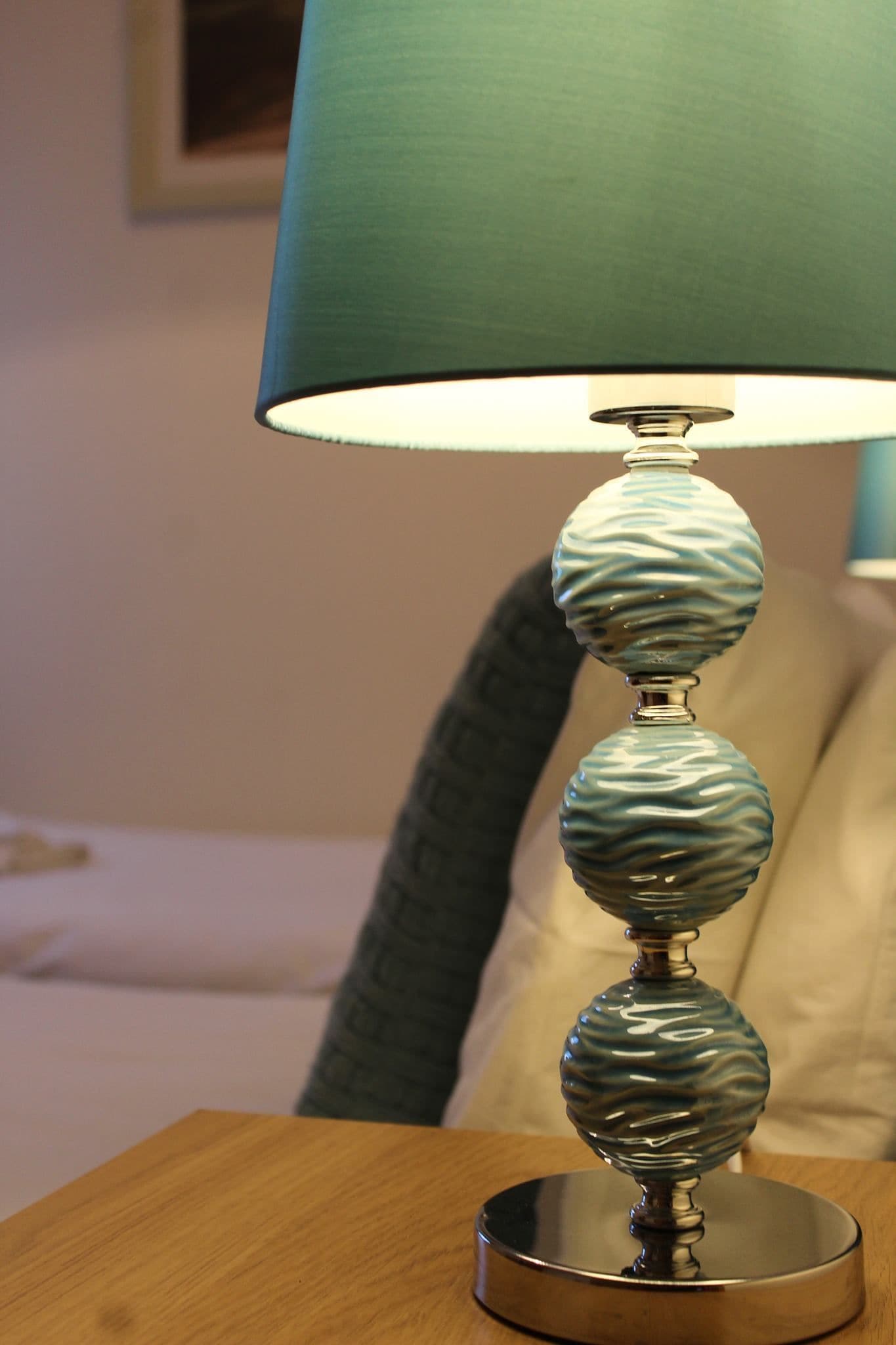A table lamp with a textured base and a teal lampshade on a wooden table.