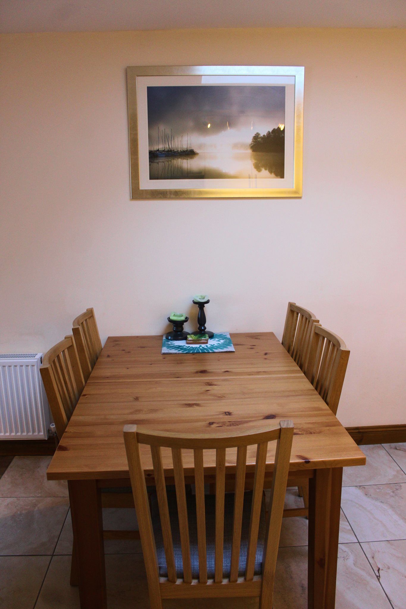 Una mesa de comedor con seis sillas de madera, un cuadro enmarcado encima y una pequeña decoración en el centro.