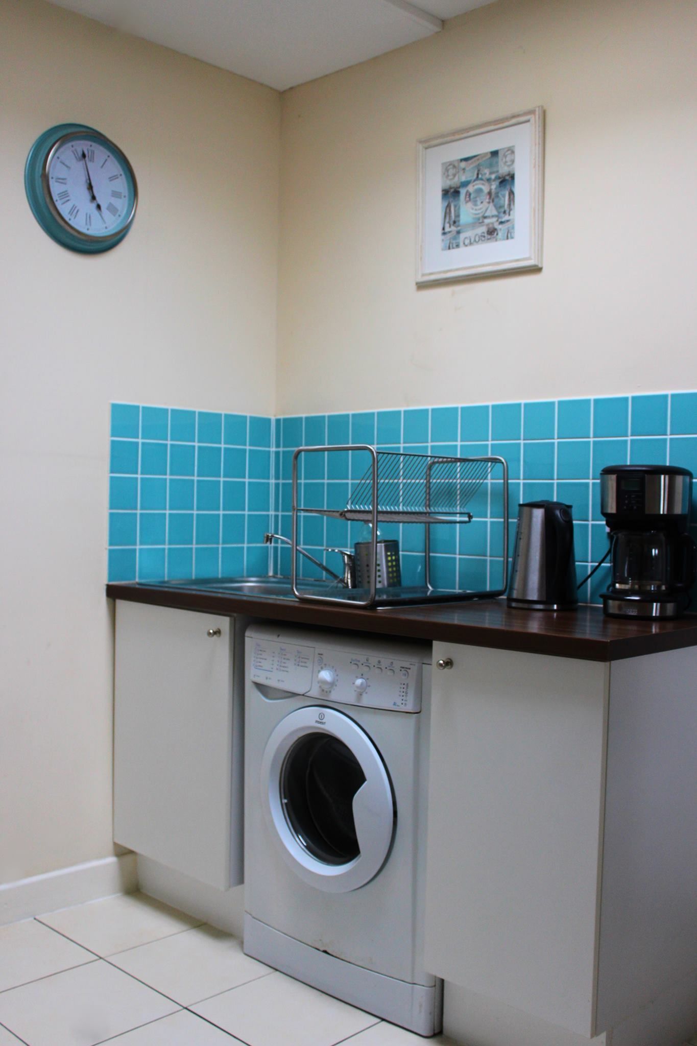 Una cocina compacta con lavadora, cafetera y un reloj en la pared.