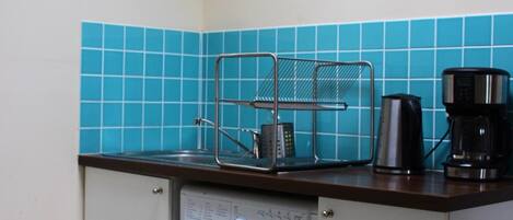 Una cocina compacta con lavadora, cafetera y un reloj en la pared.